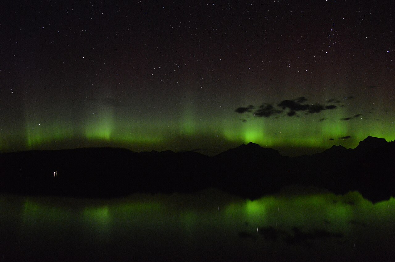 A green auroral curtain across the night sky reflected on a lake (Glacier National Park, USA).