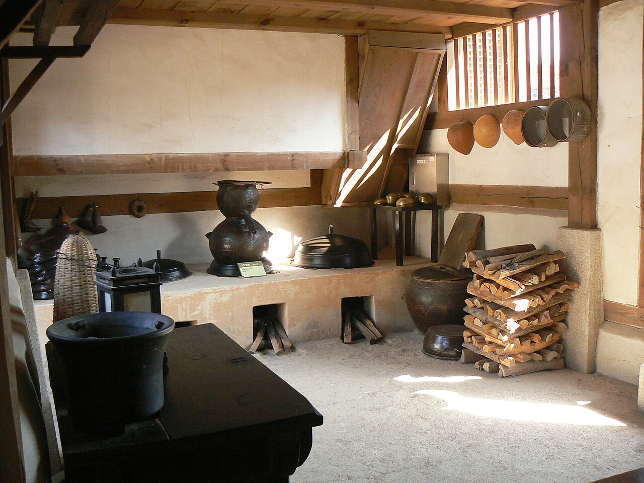 Firebox openings beneath the cooking hearth of a hanok kitchen, with a stack of firewood beside them