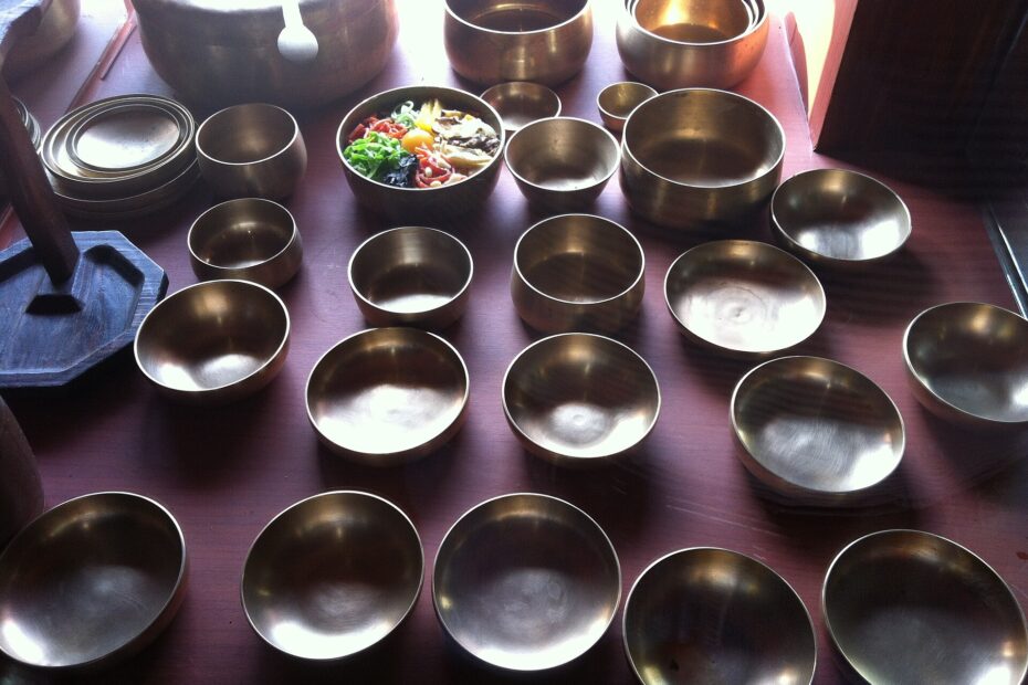 Rows of bangjja yugi bronze bowls of various sizes on a table, one of them filled with bibimbap