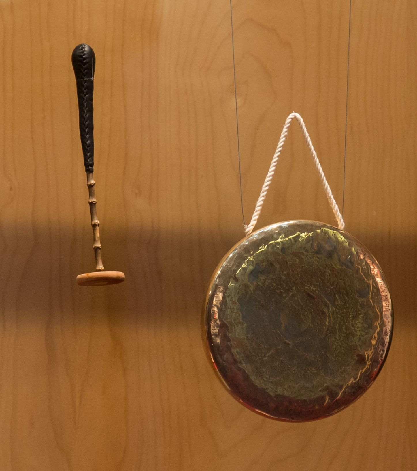 A brass-coloured kkwaenggwari gong and its beater hanging on a wooden wall