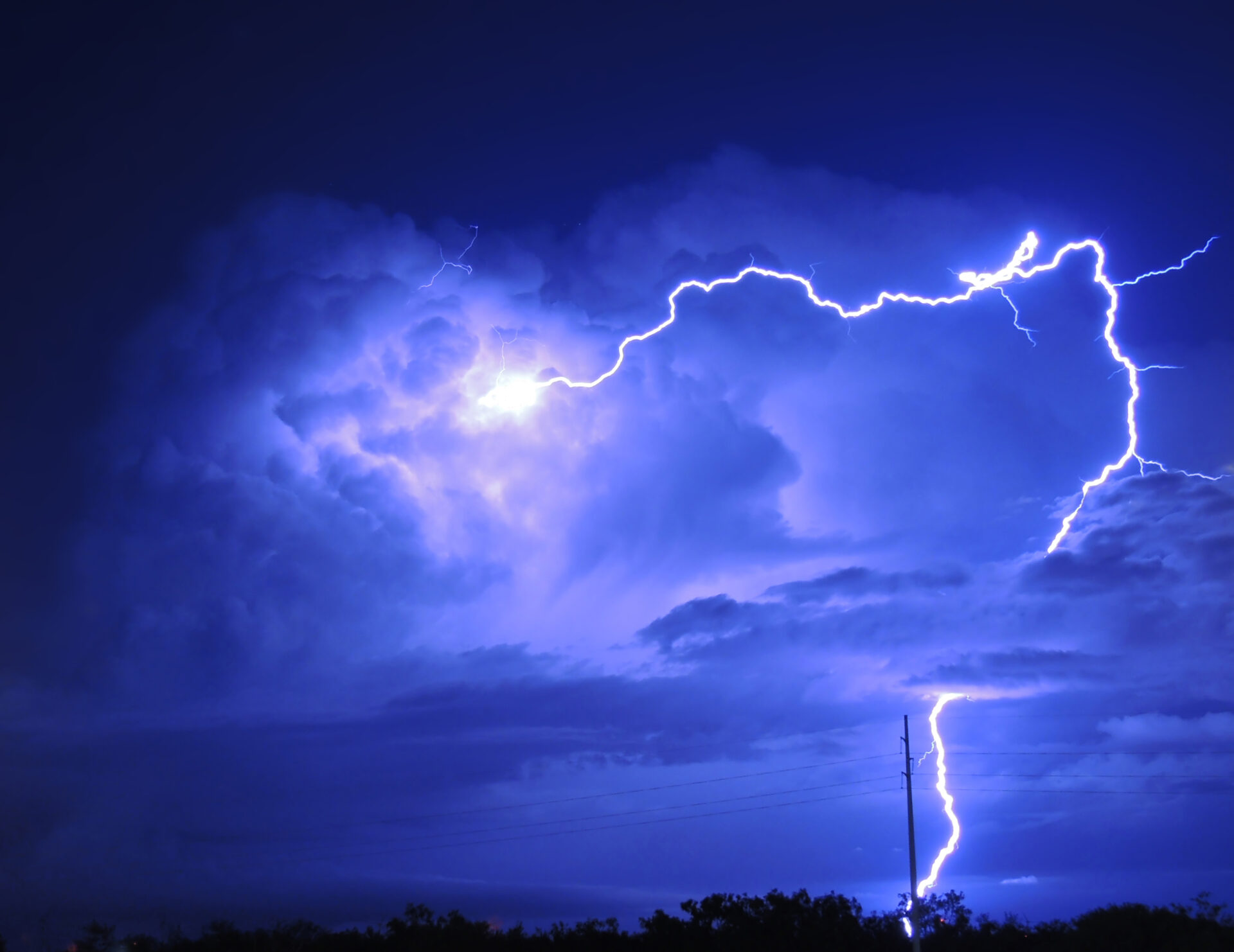 A well-developed cumulonimbus cloud in a night sky, with a thick bolt of lightning striking through it
