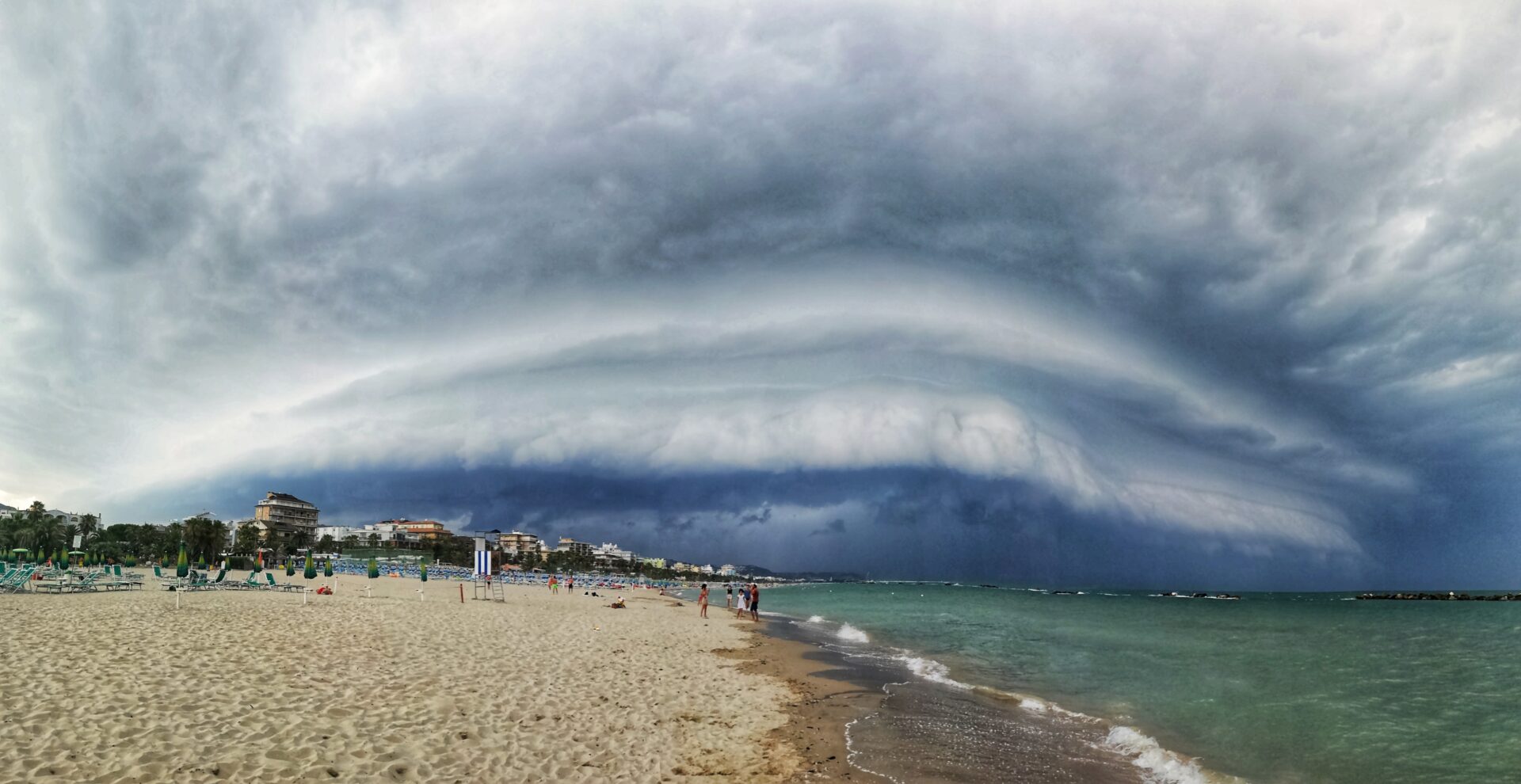 A low, elongated dark shelf cloud rolling in over a coastline
