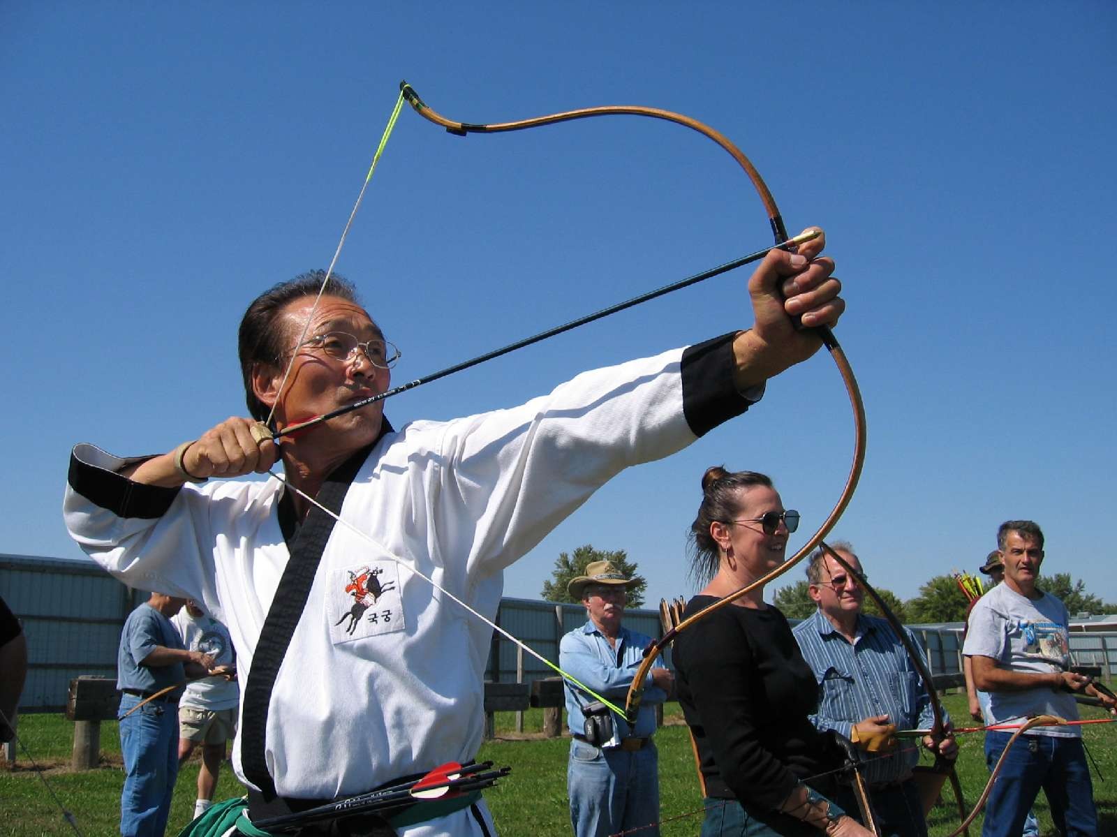 An archer in a white uniform drawing a bowstring back beside his face