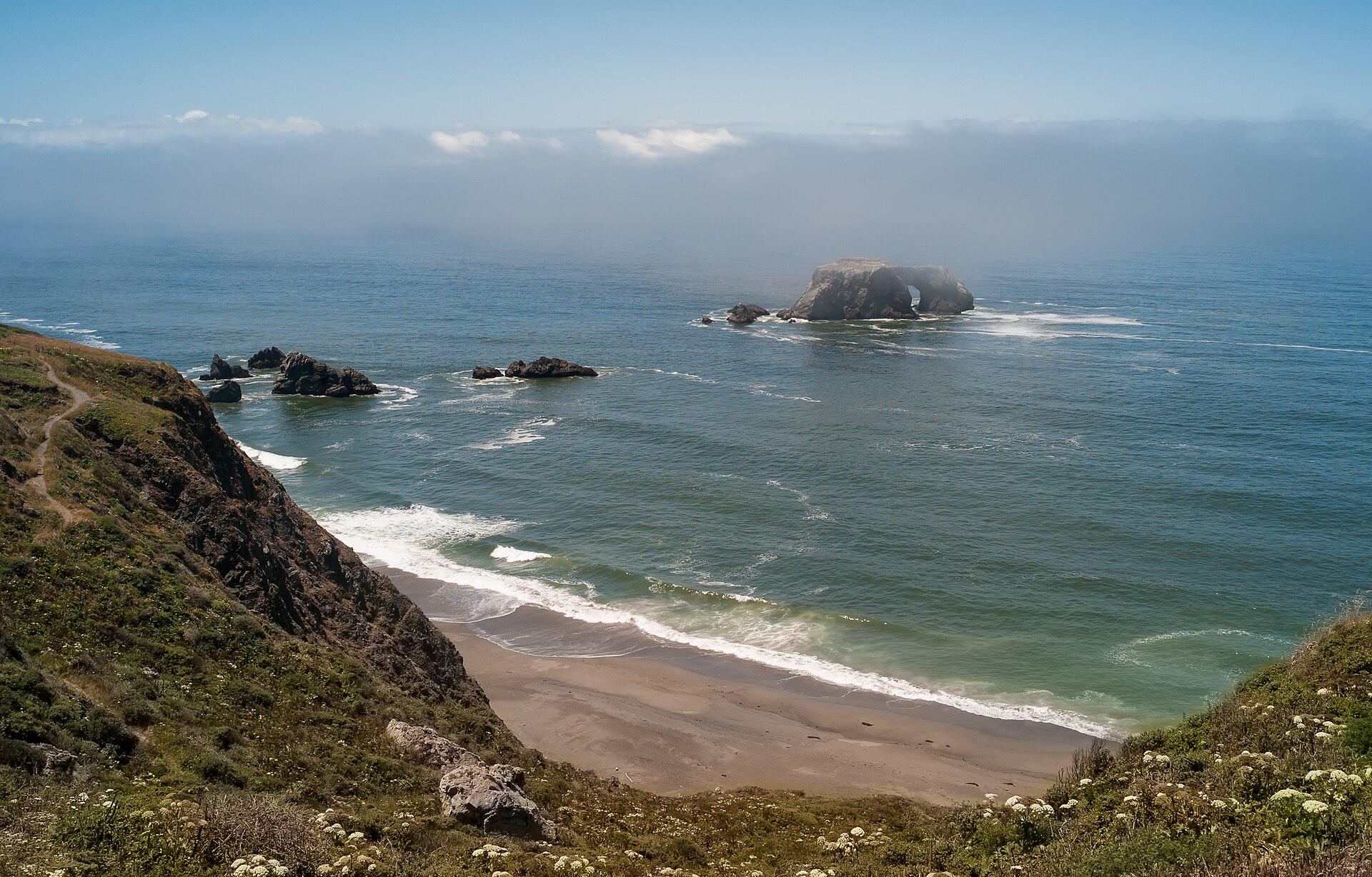 A fog bank behind Arched Rock, with coastal cliffs and waves in California