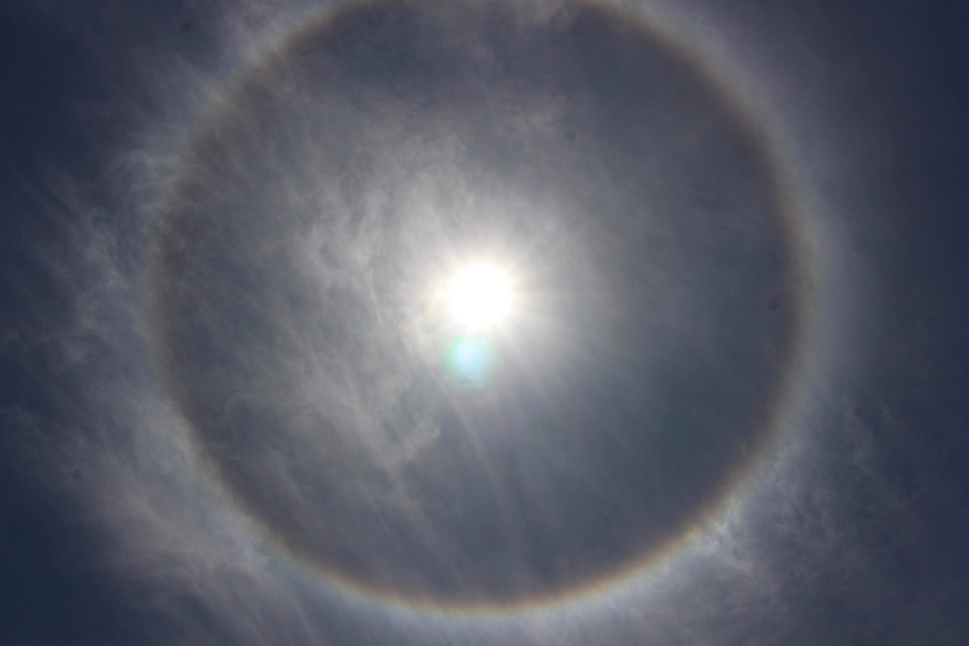 A solar halo with faint colors along the lower edge of the ring
