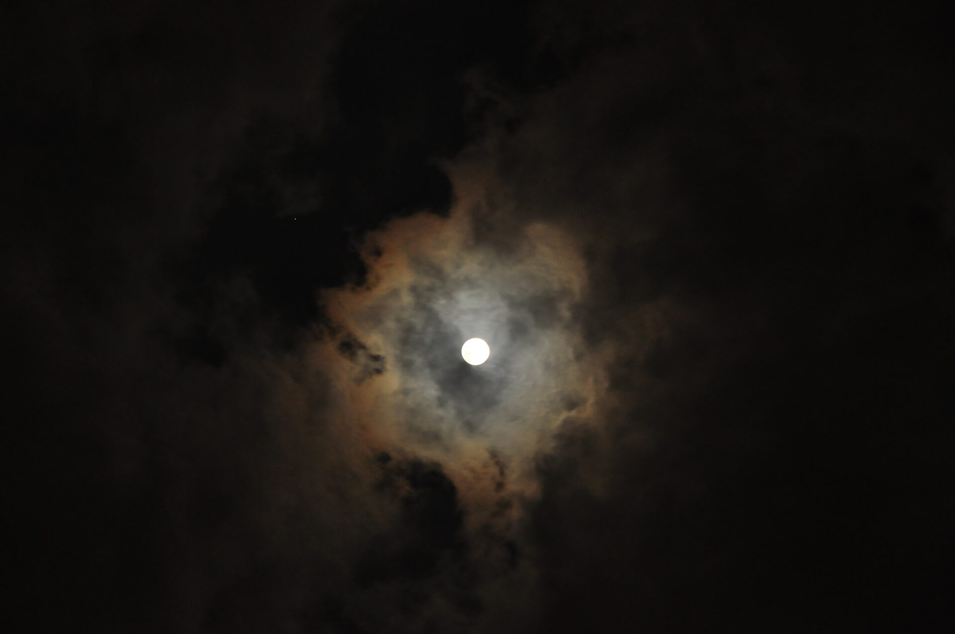A reddish-edged corona close to the Moon among clouds