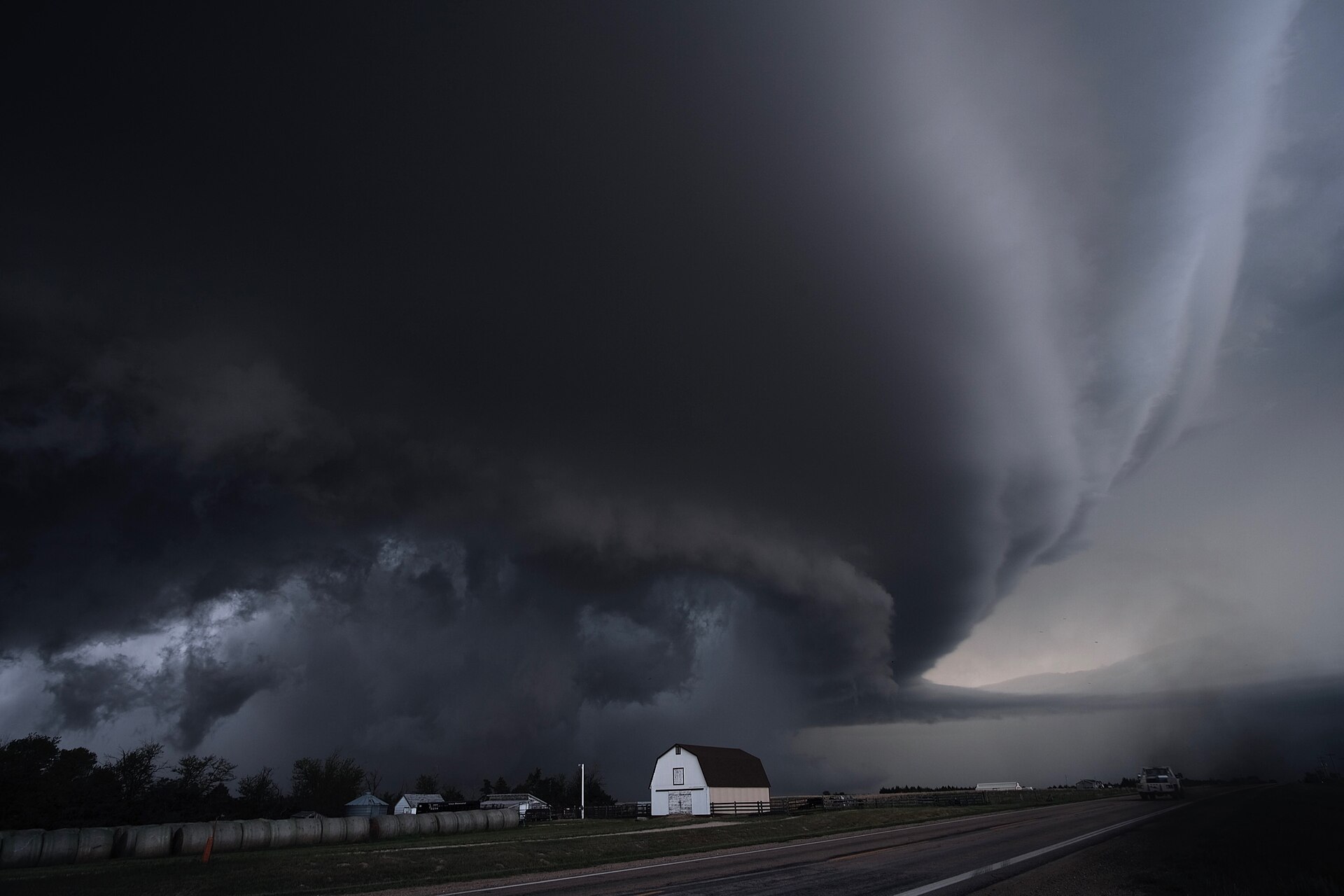An immense dark supercell thunderstorm cloud over a farm and road in Kansas