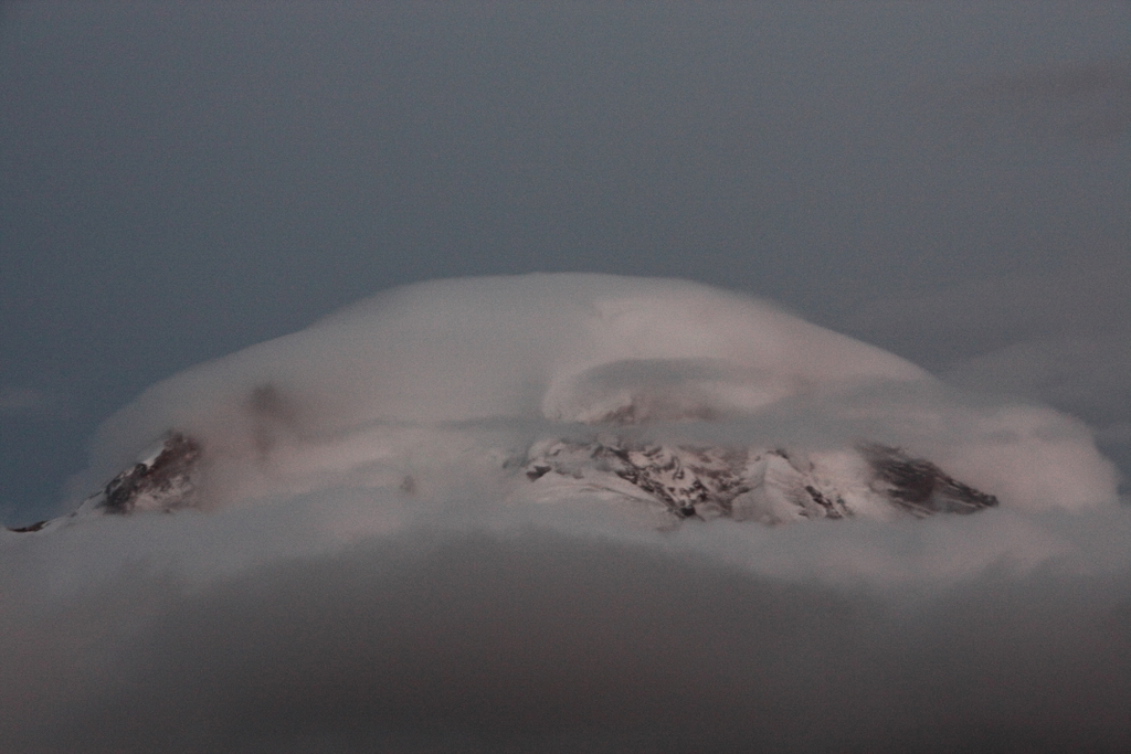 A rounded gray cloud draped like a cap over the snow-covered summit area of Mount Baker