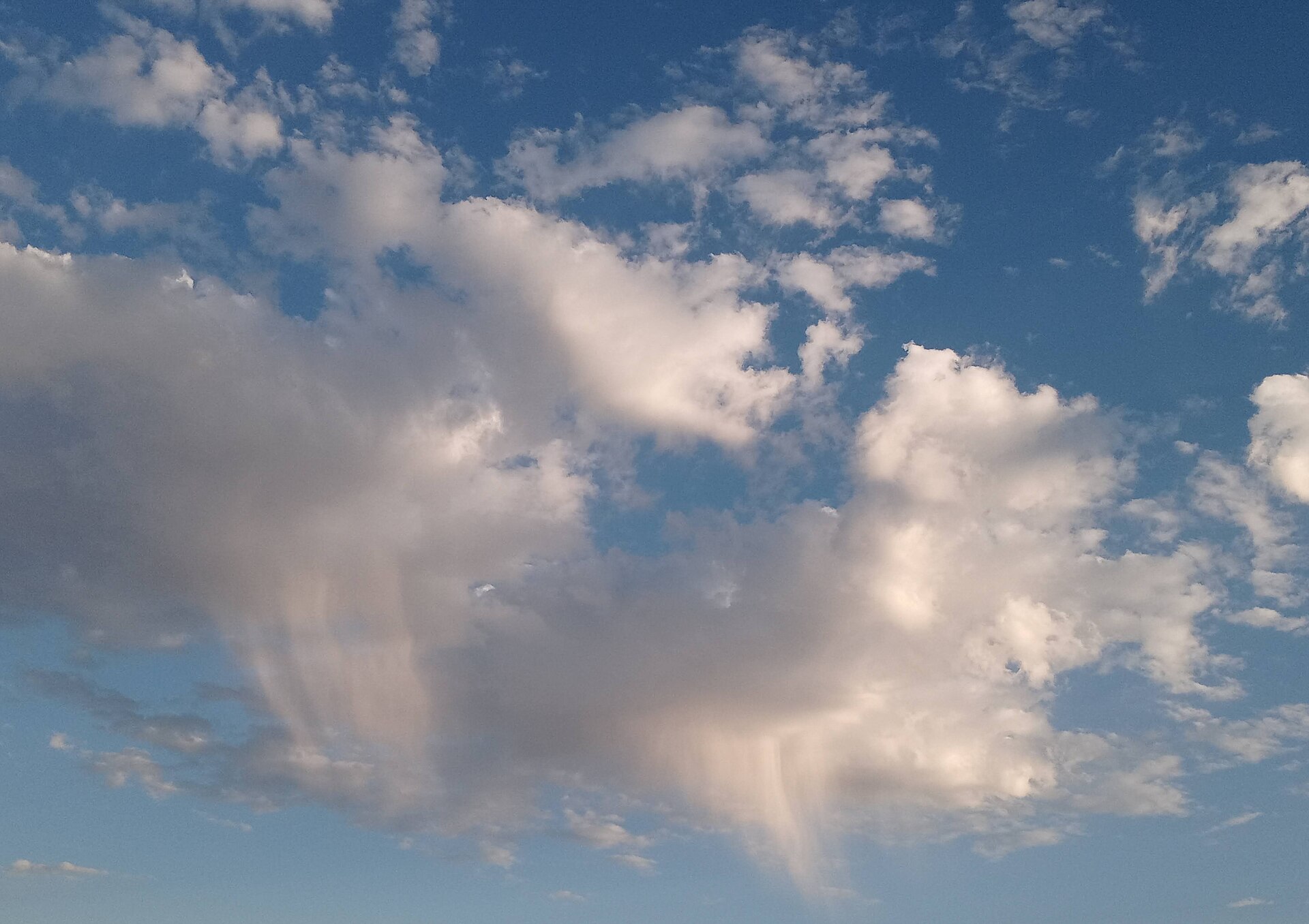 Faint precipitation trails extending below two clouds in a blue sky