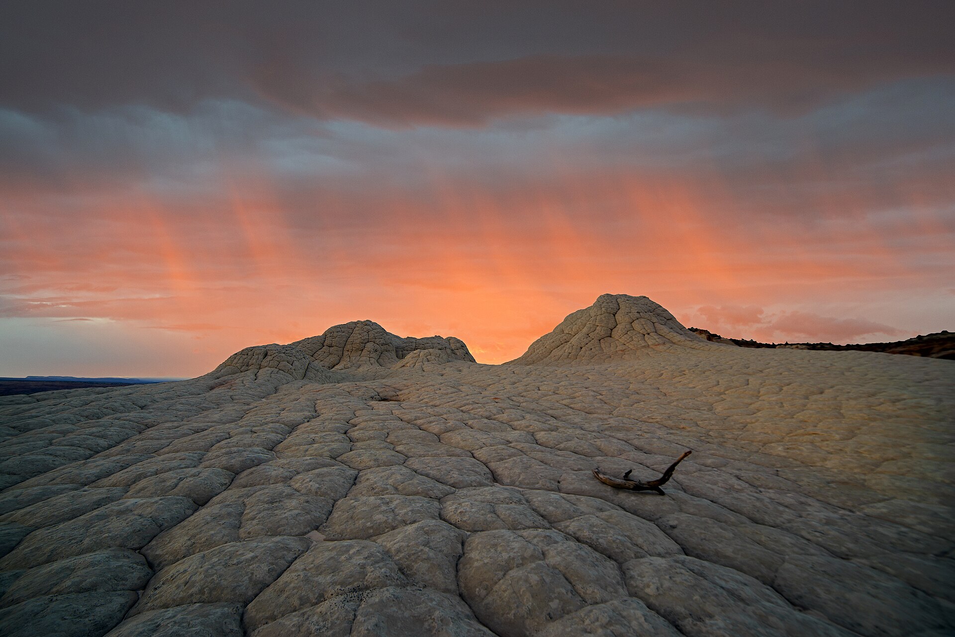 Sunset-colored precipitation streaks over dry rocky terrain