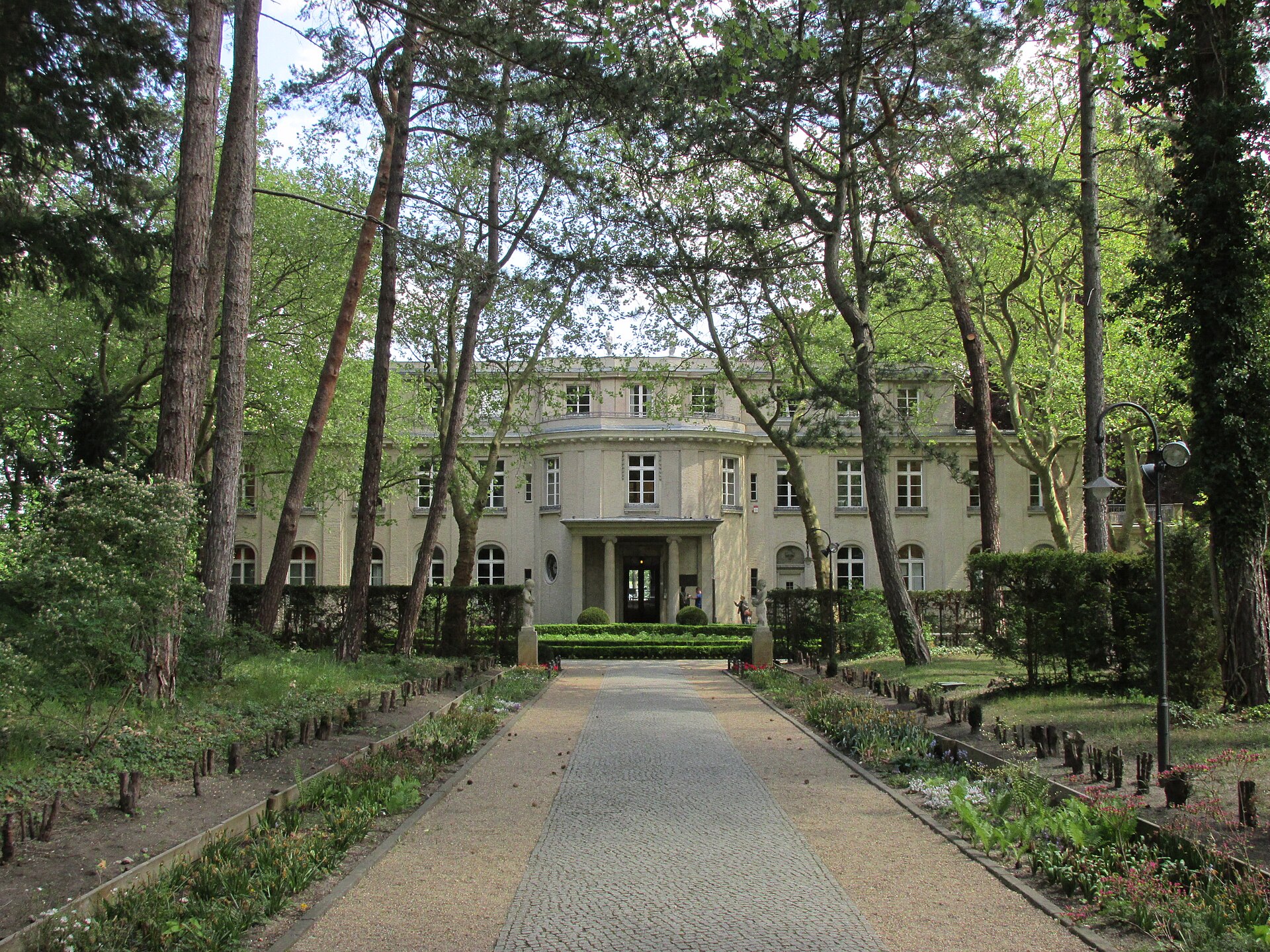 The front of a white two-story villa at the end of a tree-lined path.