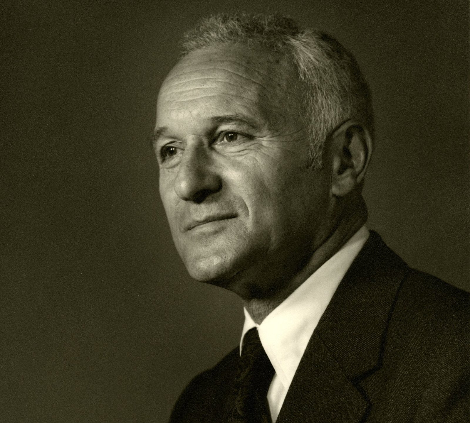 Black-and-white portrait of a gray-haired man in a white shirt and tie, looking off to one side