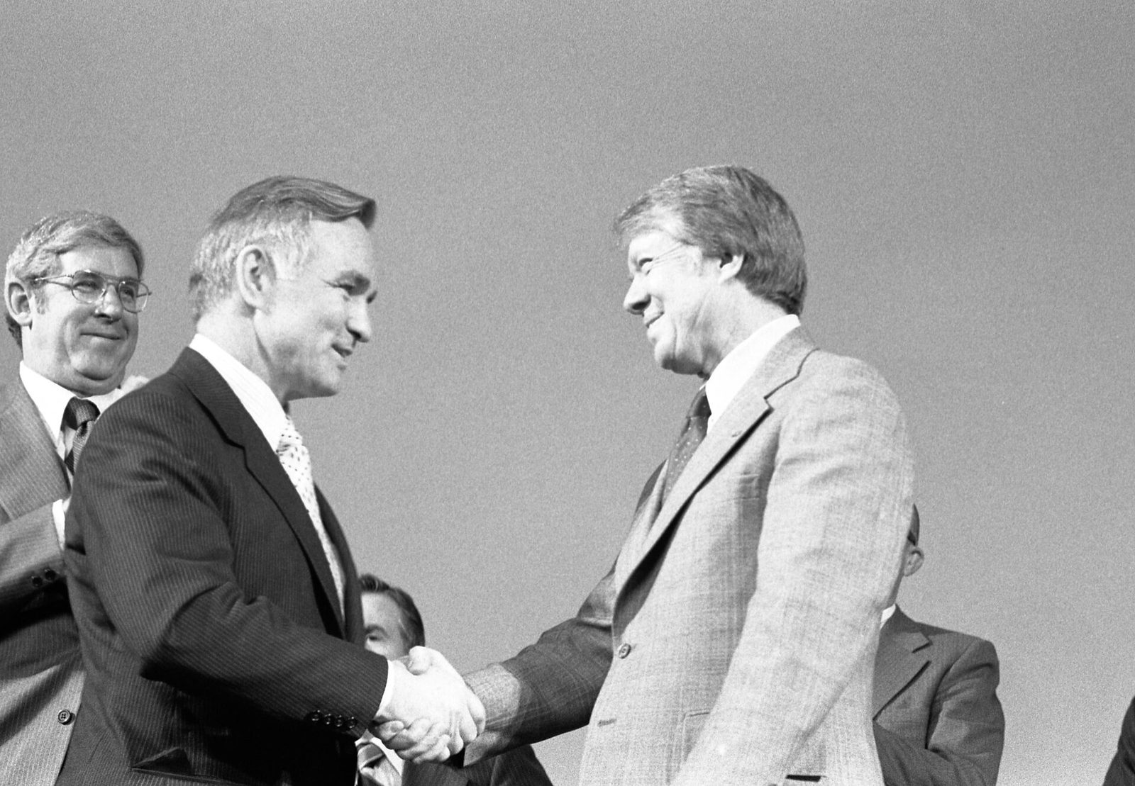 Black-and-white photograph of two men in suits smiling and shaking hands at an outdoor ceremony